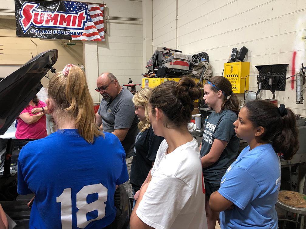 Students gathered around a car looking under the hood