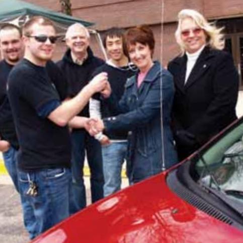People shaking hands in front of a red car