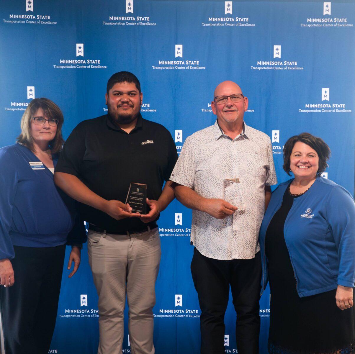 4 people standing in front of a blue backdrop holding awards